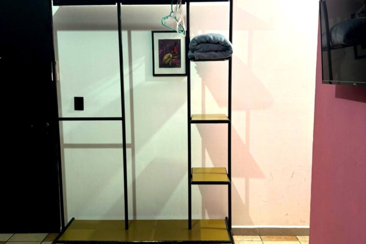 A room with a bed, a wardrobe, a shelf unit, and a TV on the wall.