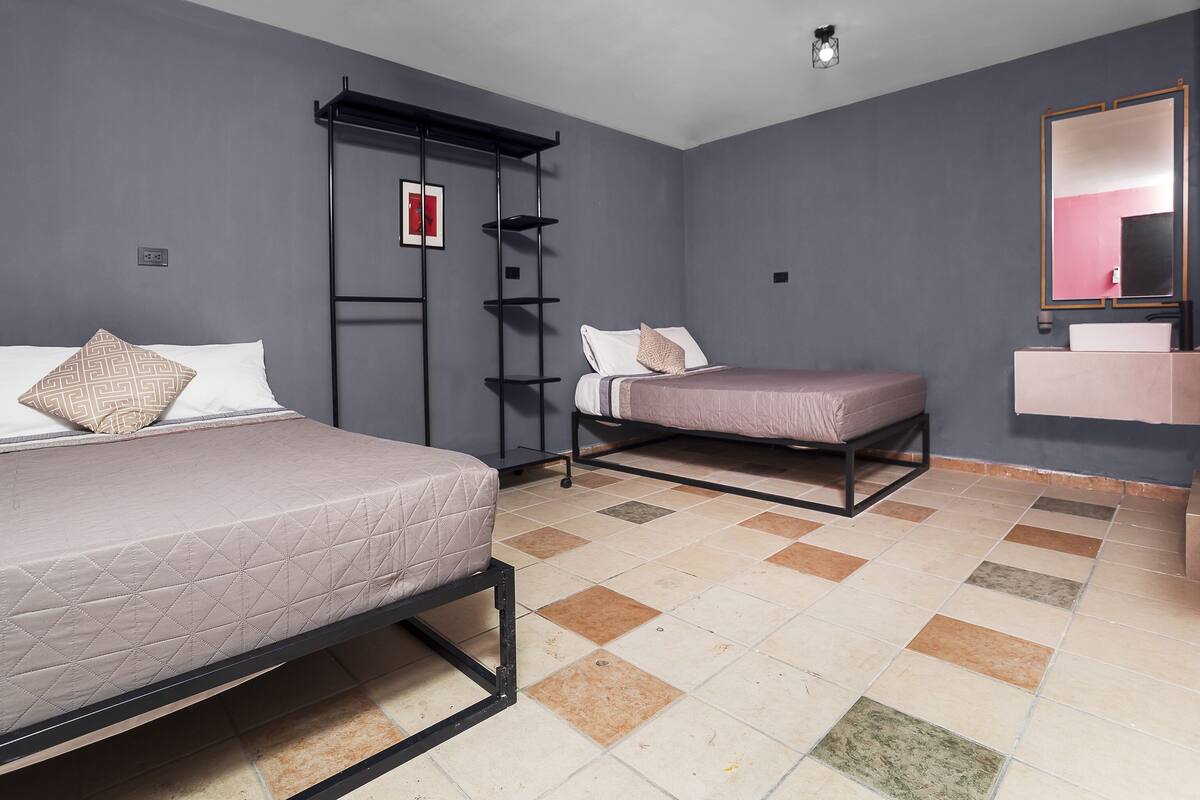 A bedroom with two beds, a wardrobe, a mirror, and a tiled floor.