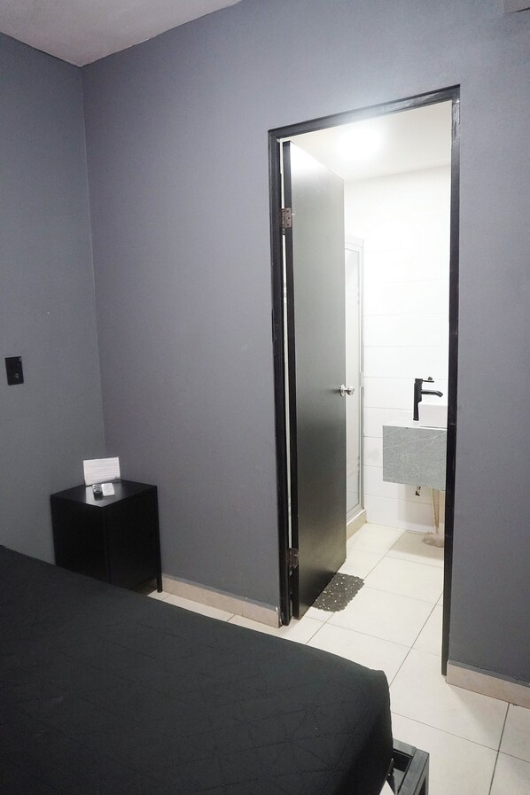 A hotel room with a bed, a small bedside table, a door leading to a bathroom, and a tiled floor. - Adhoc Cintermex (Monterrey)
