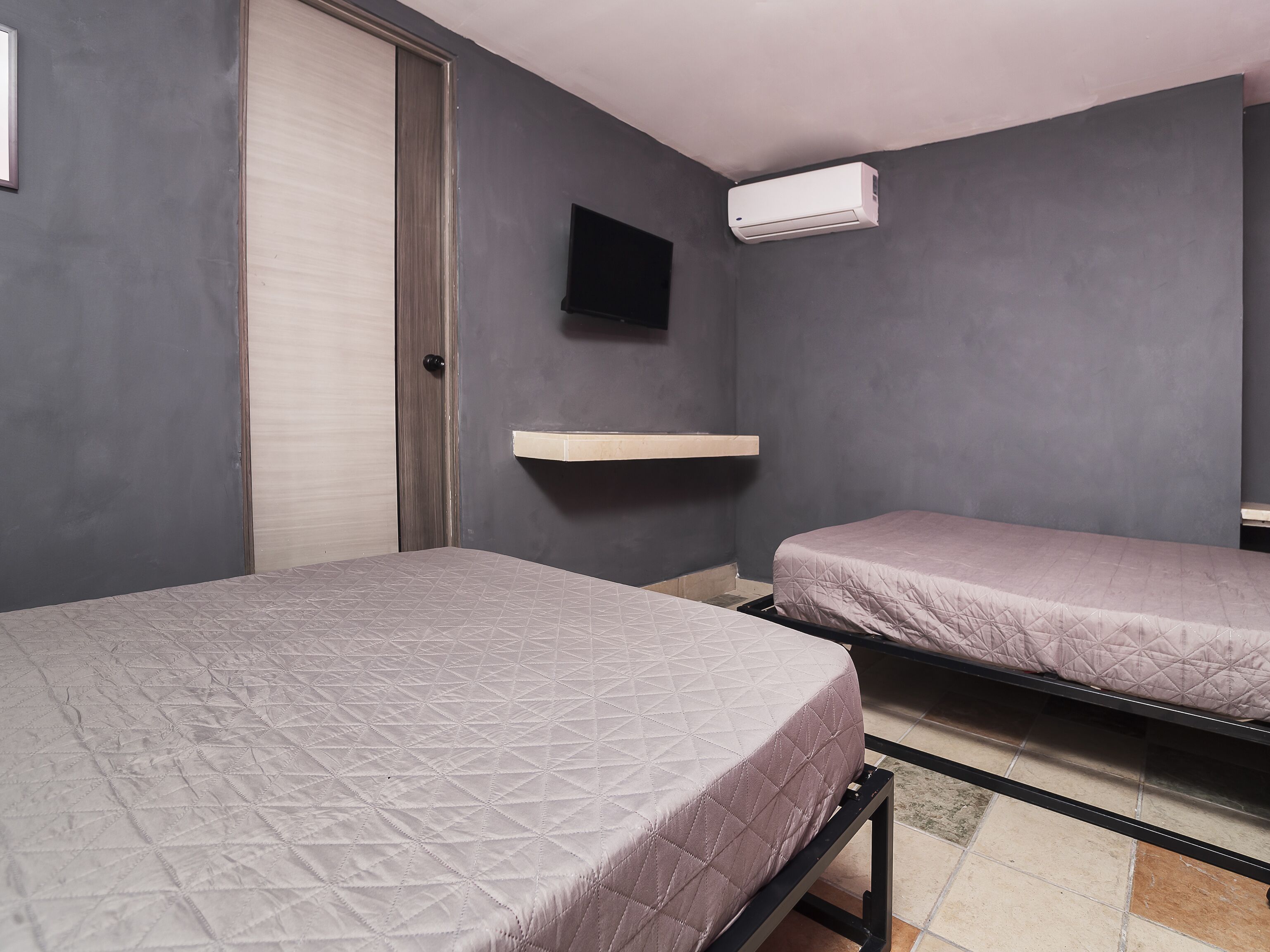 Un dormitorio con dos camas, un televisor montado en la pared y un equipo de aire acondicionado.