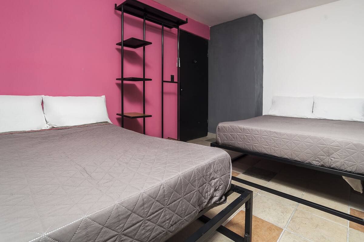 A room with two beds, a pink wall, a black shelf unit, and a grey door.