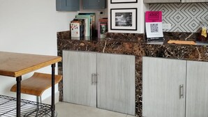 A kitchen with a marble countertop, grey cabinets, a wooden table, and a QR code on the wall. - Adhoc Cintermex (Monterrey)