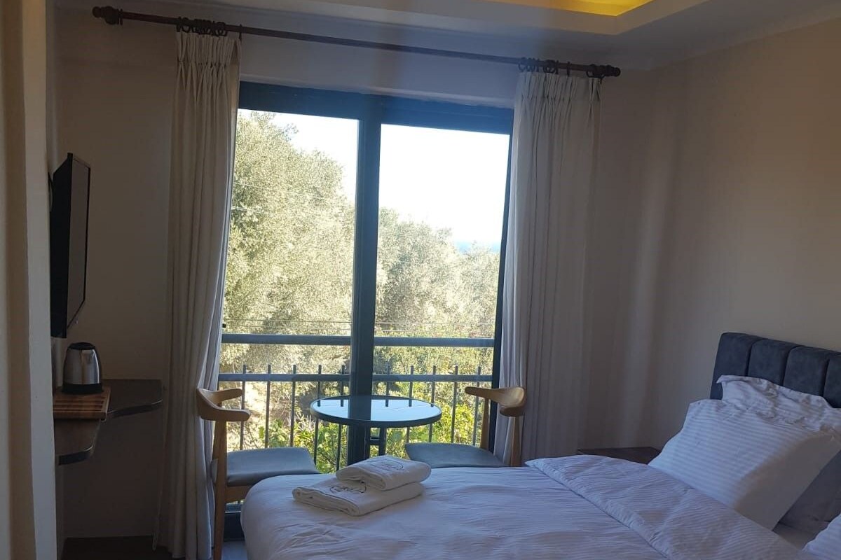 Une chambre d’hôtel avec un grand lit, un bureau et un balcon donnant sur la forêt.