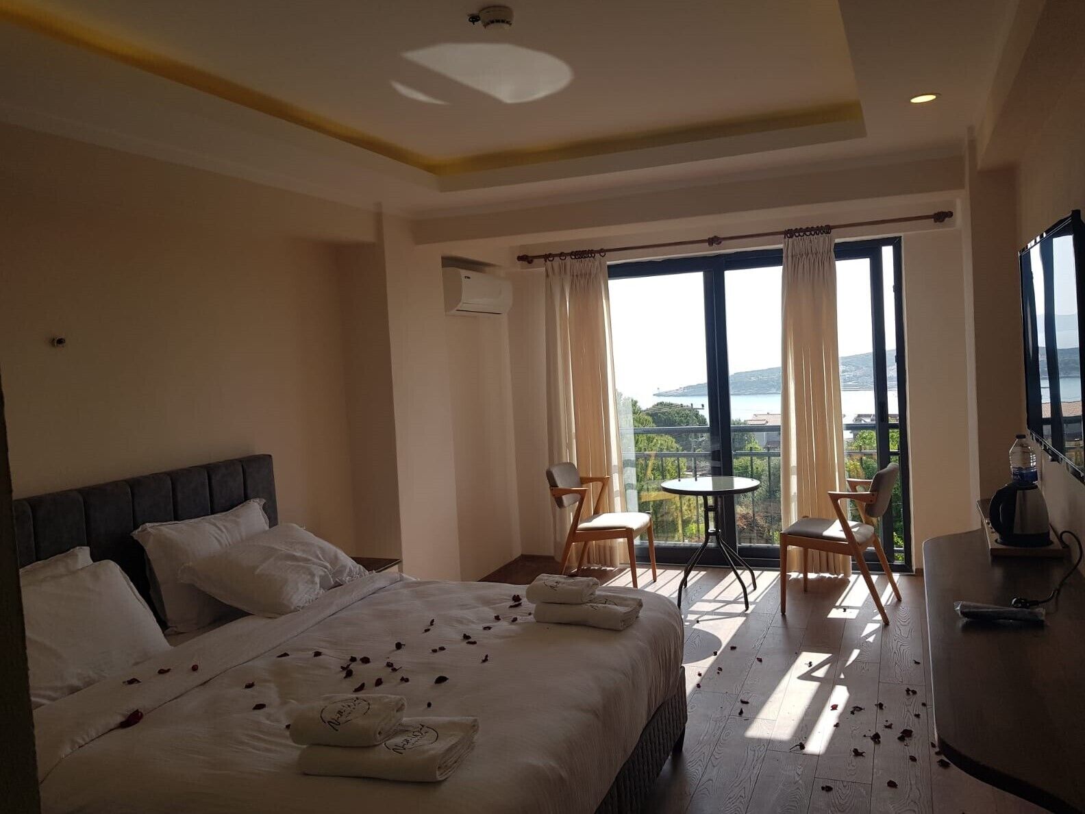 A hotel room with a bed, a balcony with a table and chairs, and a view of the sea.