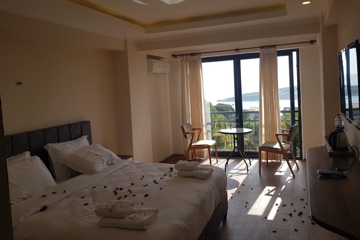 Un cuarto de hotel con una cama, un balcón con mesa y sillas, y vista al mar.
