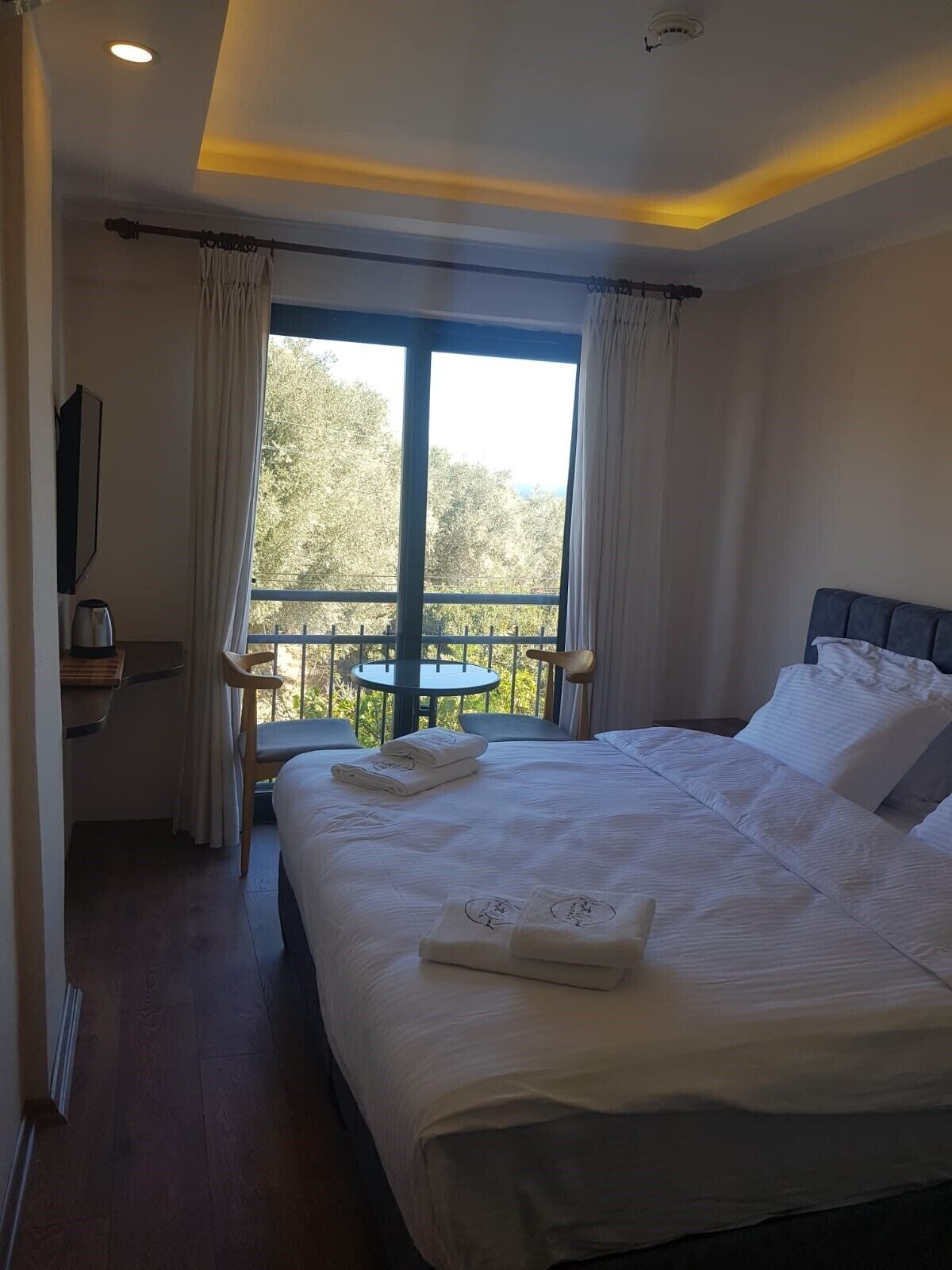 A hotel room with a large bed, a desk, and a balcony with a view of trees.