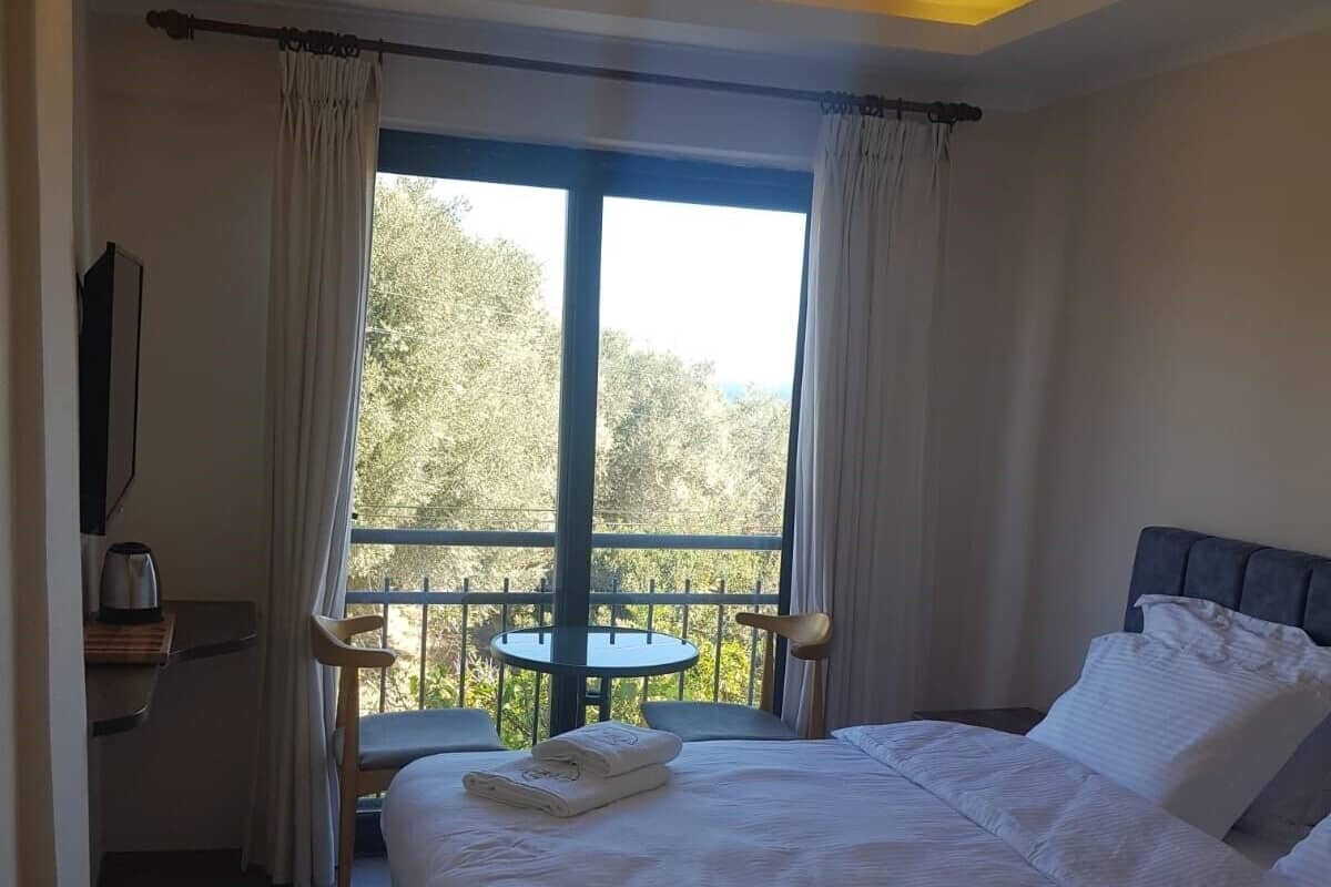 Habitación de hotel con una cama grande, un escritorio y un balcón con vistas a árboles.