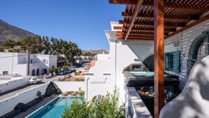 A poolside area with a view of a mountain, a white building, and a pergola structure. - Armonia (Santorini)