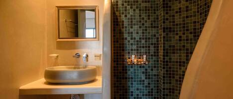 Ein modernes Badezimmer mit einem großen Waschbecken, einem Spiegel und einer Dusche mit Mosaikfliesen.