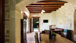 A rustic interior with a wooden dining table, stone walls, and a view of an outdoor swimming pool.