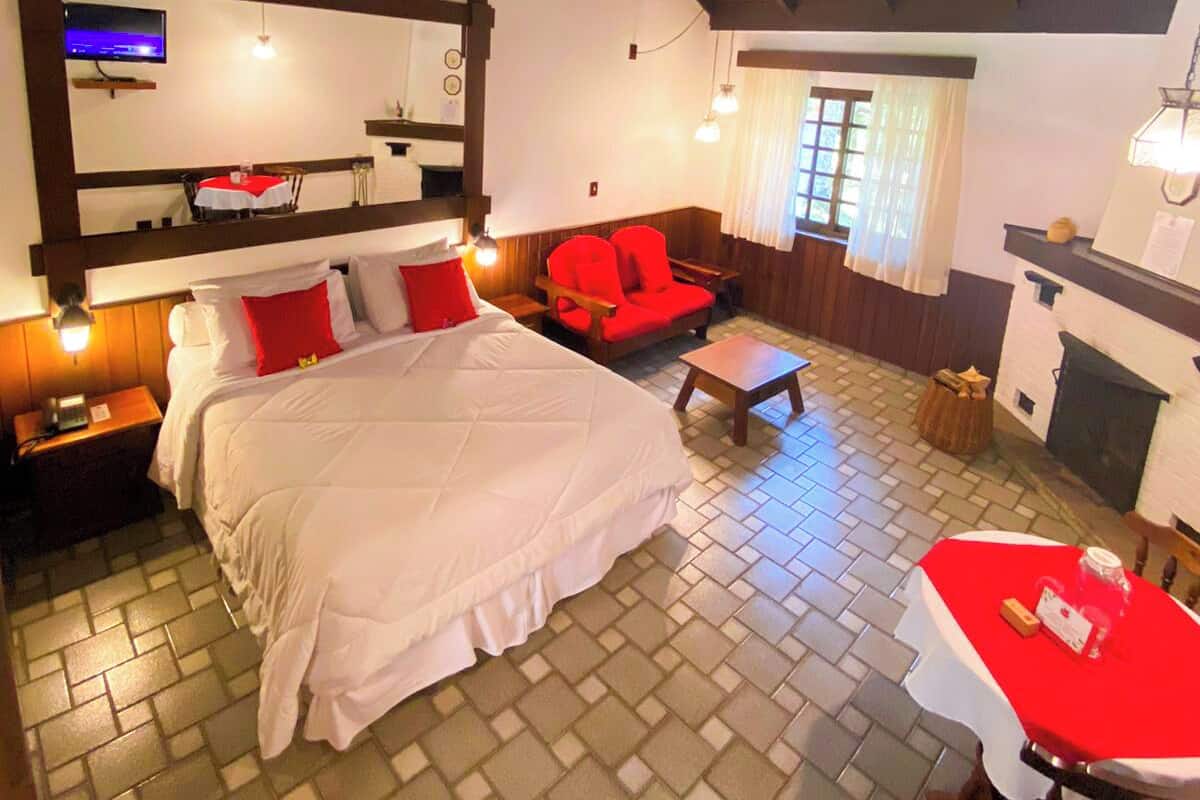 Una habitación acogedora con una cama grande, una silla roja, una mesita, un televisor y una chimenea.