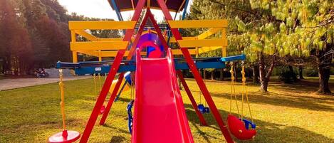 A playground with a red slide, yellow and blue structures, and trees in the background.