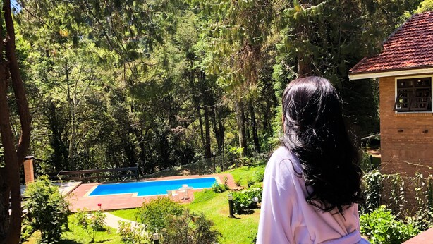 A person overlooking a backyard with a swimming pool, a brick house, and a wooden deck.