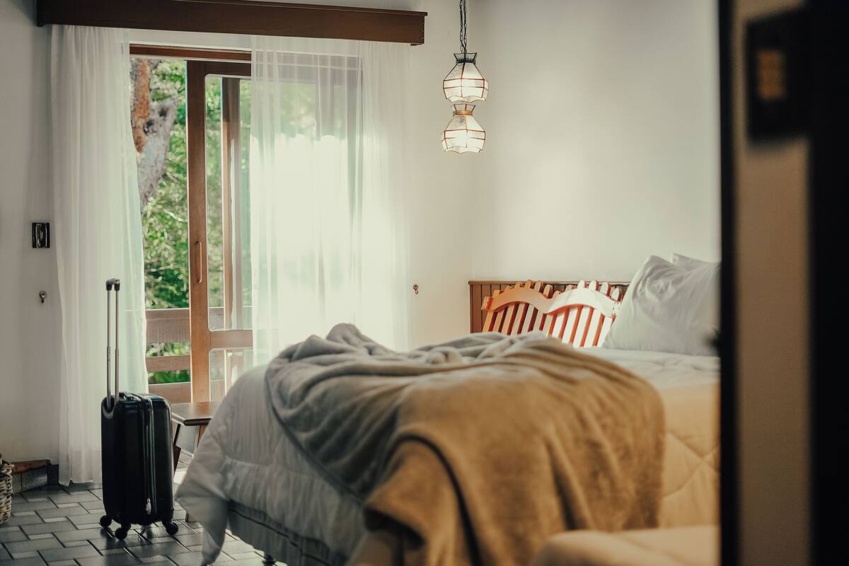 Un dormitorio con cama, maleta, cabecero de madera y lámpara colgante.