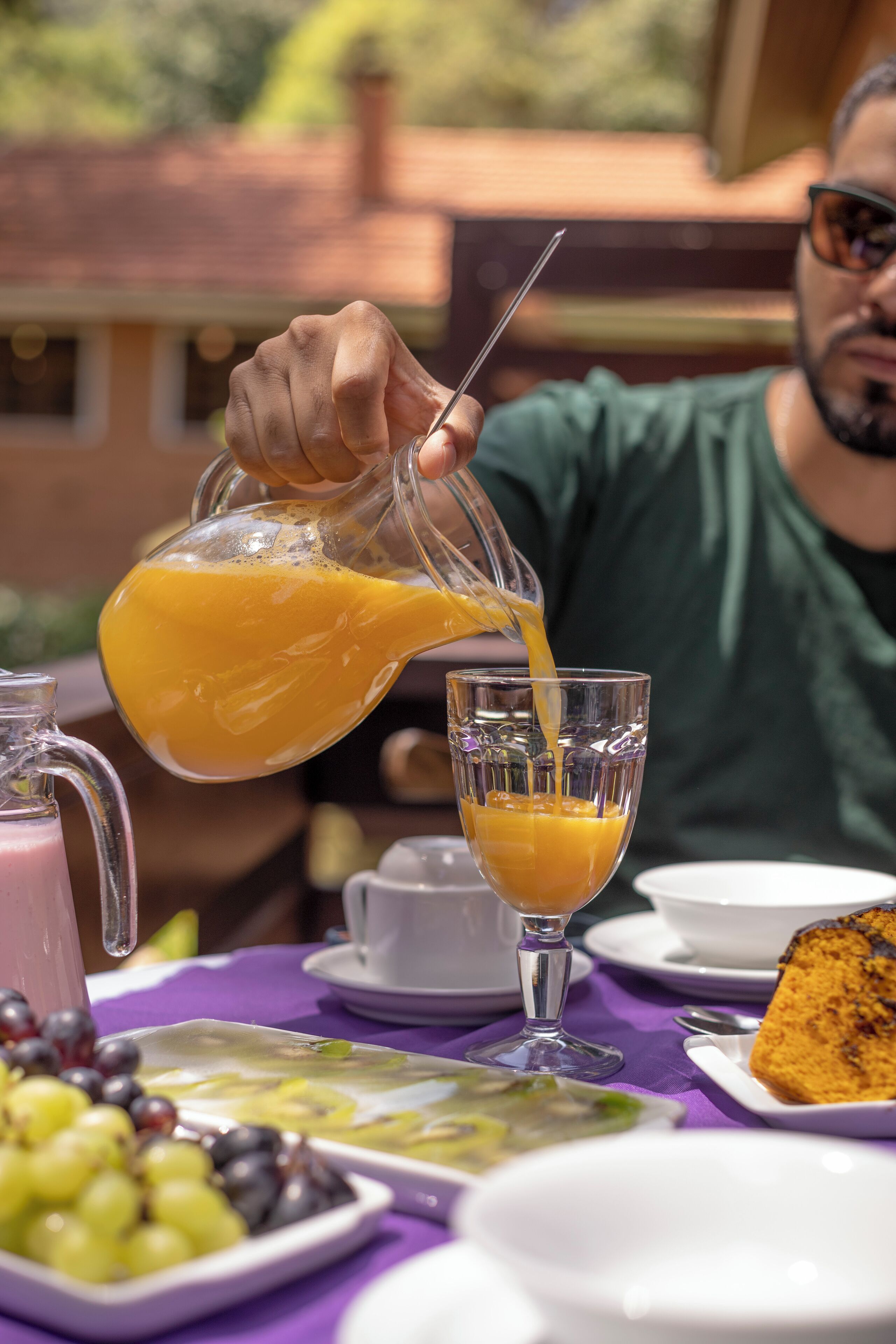 A breakfast setting with a glass of orange juice being poured, a plate of grapes, and a slice of cake on a table.
