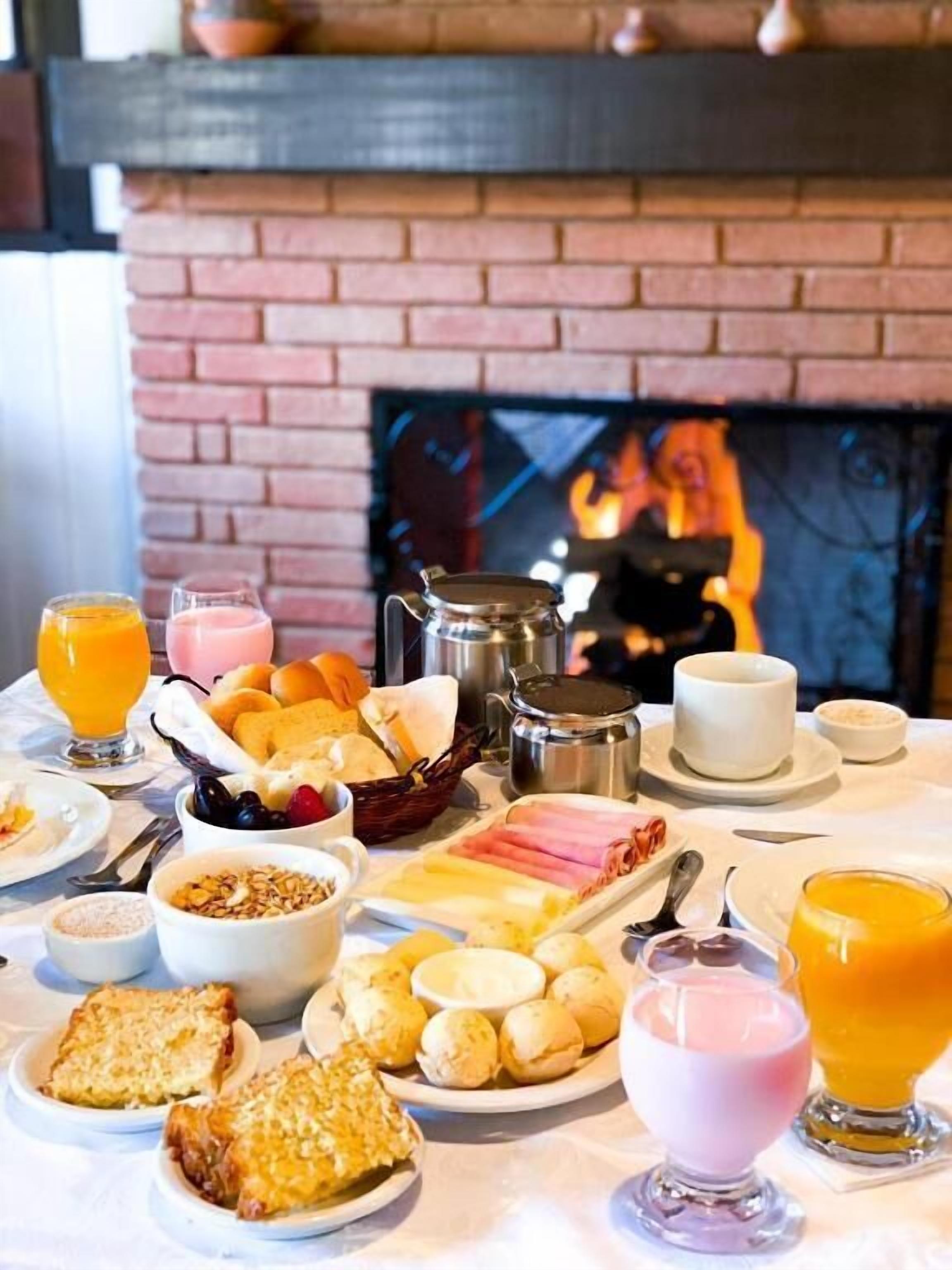 Een ontbijtbuffet met diverse gerechten en dranken, een open haard op de achtergrond en een bakstenen muur.