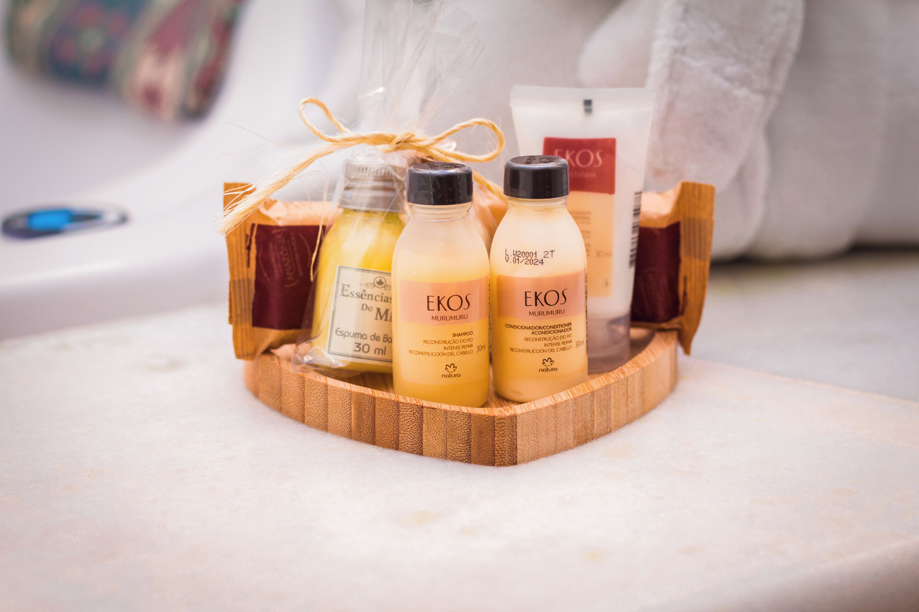 Een houten dienblad met drie flesjes shampoo en conditioner, en een witte fles lotion, allemaal van het merk 'EKOS'.