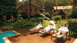 A wooden deck with lounge chairs, a swimming pool, and a house surrounded by greenery.