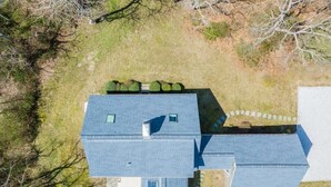 A two-story house with a sloped roof, a small attached garage, and a fenced yard. - Book Eastham, Plenty Of Room For Entire Family! (Eastham)