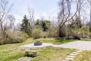 A paved outdoor area with a circular stone fire pit, a stone bench, and a paved walkway. - Book Eastham, Plenty Of Room For Entire Family! (Eastham)