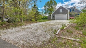 A residential property with a gravel driveway, a garage, and a house surrounded by trees. - Book Eastham, Plenty Of Room For Entire Family! (Eastham)