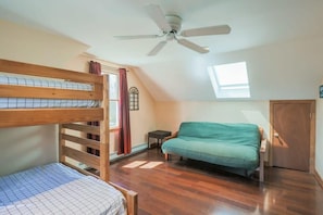 A dorm-style room with a bunk bed, a single bed, a sofa, a ceiling fan, and a window.