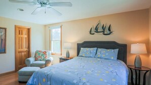 A bedroom with a bed, a chair, a nightstand, a lamp, a ceiling fan, and a window. - Book Eastham, Plenty Of Room For Entire Family! (Eastham)