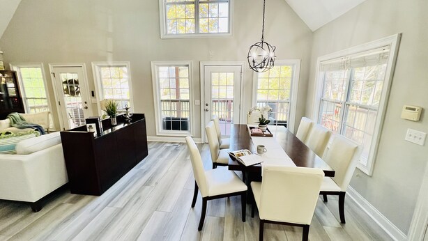 A spacious dining area with a high ceiling and large windows, a dark wood dining table, and white upholstered chairs. - Southern Living Lake Oconee Home in a Cove! (Buckhead)