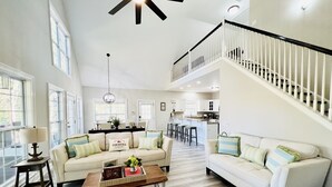 A spacious living area with a high ceiling, a staircase, and a kitchen in the background. - Southern Living Lake Oconee Home in a Cove! (Buckhead)
