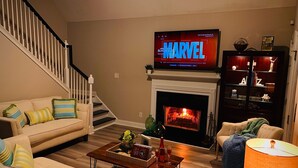 A living room with a fireplace, a television displaying 'Marvel', and a staircase. - Southern Living Lake Oconee Home in a Cove! (Buckhead)