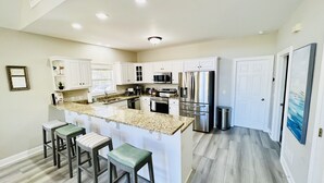 A modern kitchen with white cabinets, stainless steel appliances, and a granite countertop. There are three bar stools with green cushions. - Southern Living Lake Oconee Home in a Cove! (Buckhead)
