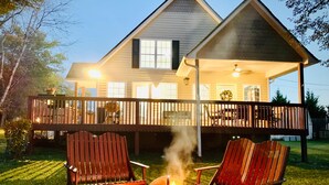 A house with a covered porch, two Adirondack chairs, and a fire pit. - Southern Living Lake Oconee Home in a Cove! (Buckhead)