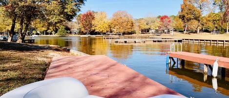 A park with a calm lake, a wooden dock, and autumn-colored trees.