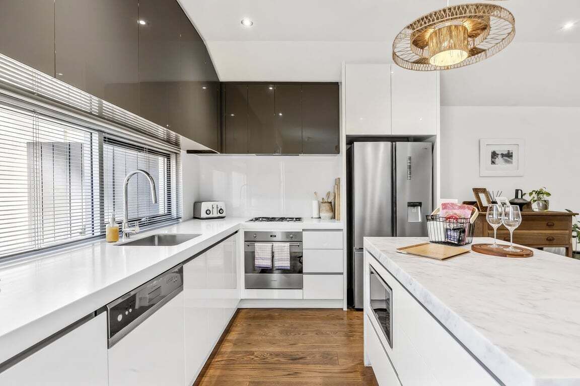 A modern kitchen with white cabinetry, stainless steel appliances, and a wooden floor.