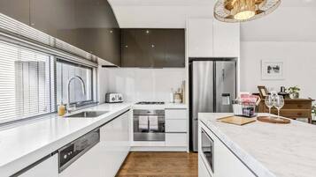 A modern kitchen with white cabinetry, stainless steel appliances, and a wooden floor.