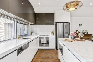A modern kitchen with white cabinetry, stainless steel appliances, and a wooden floor.