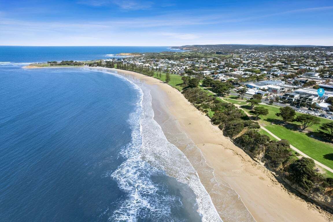 Vista aérea de uma área costeira com praia, edifícios residenciais e céu claro.