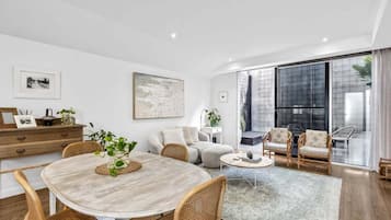 A modern living room with a dining area, large windows, and a view of the outside.