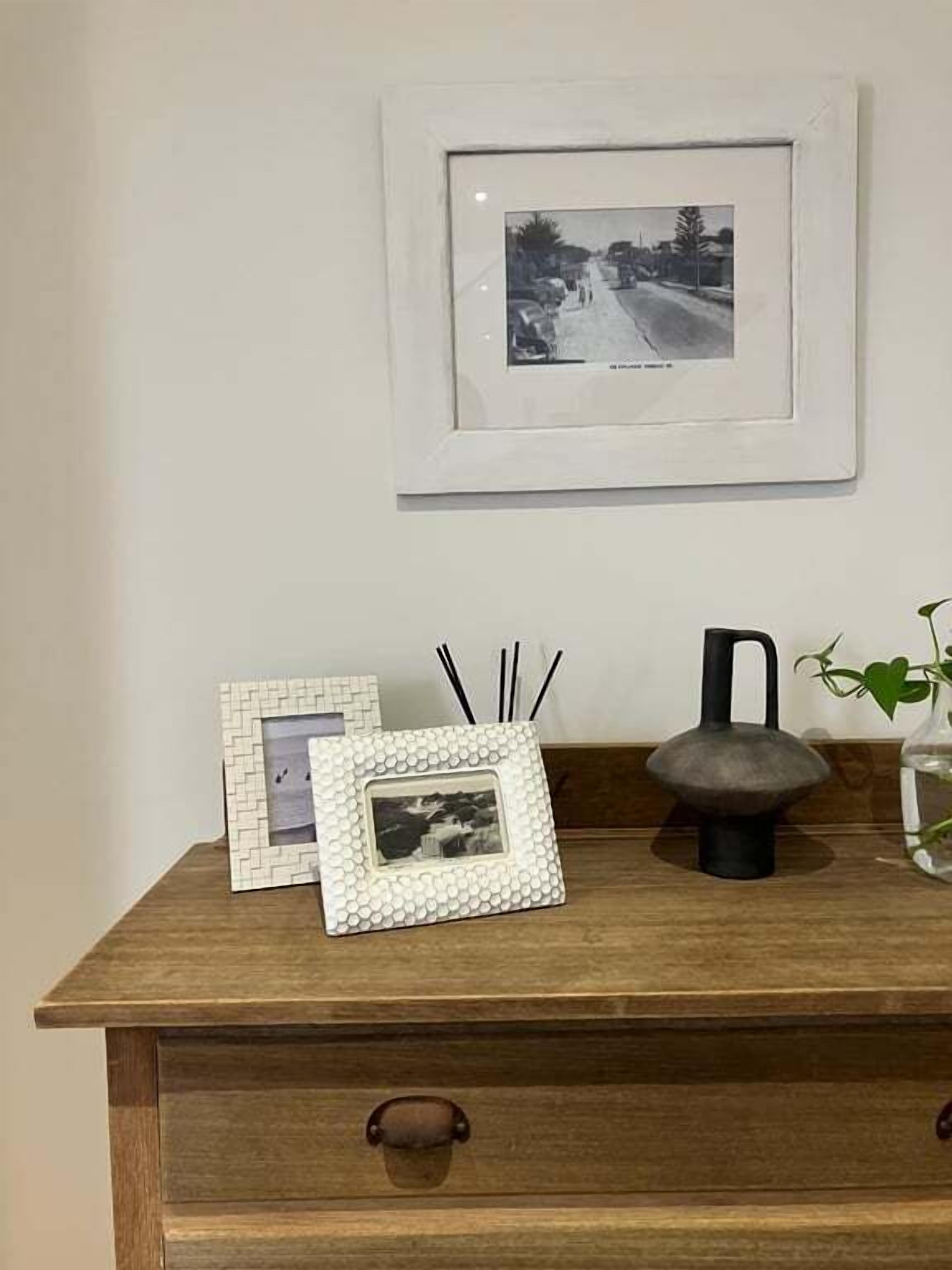 Un aparador de madera con una fotografía enmarcada, una planta pequeña en maceta y un objeto decorativo encima.