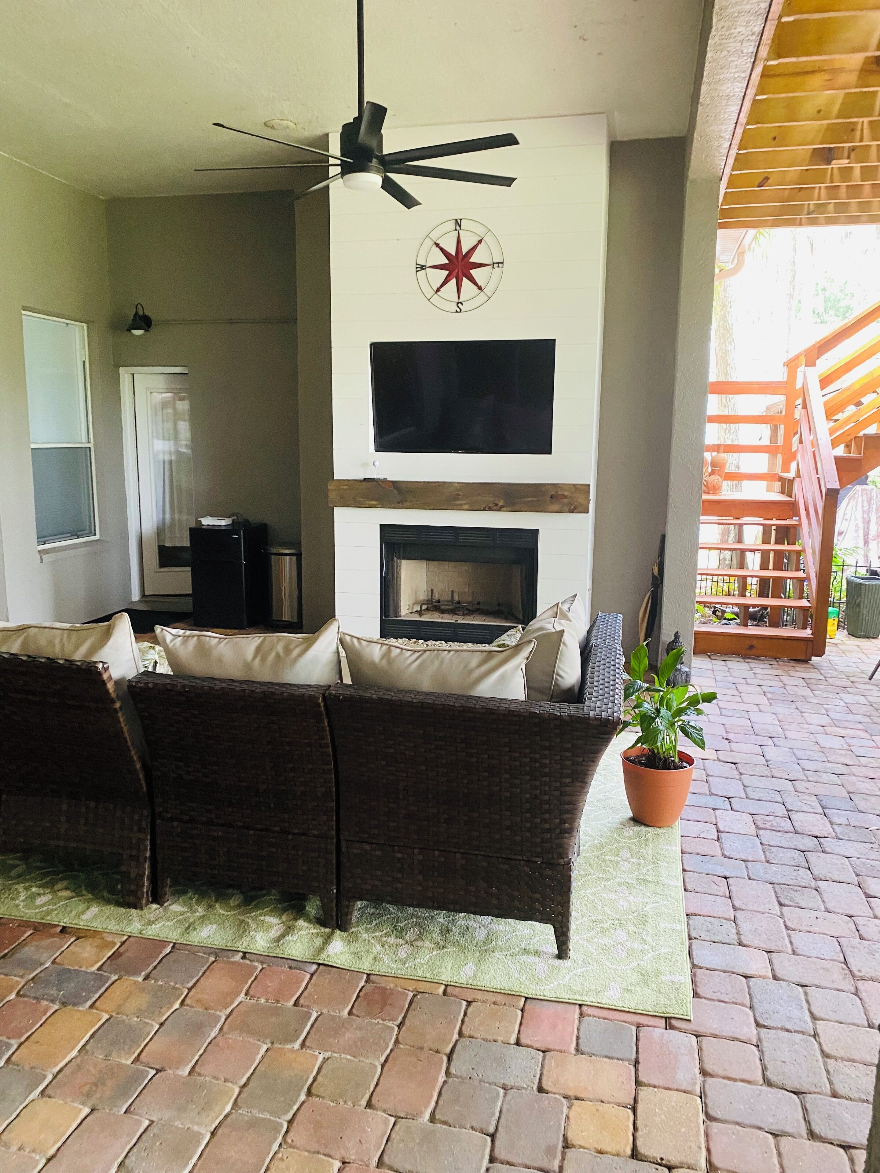 Un patio con chimenea, sofá, televisor y ventilador de techo.