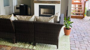 Eine Terrasse mit Kamin, einer Sitzecke, einem Fernseher und einem Deckenventilator.