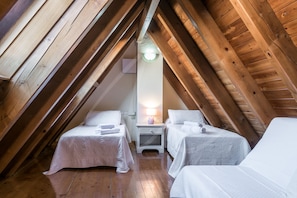 A cozy attic bedroom with two beds, wooden beams, and a nightstand with a lamp.