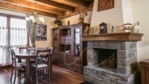 A dining area with a wooden table and chairs, a fireplace with a stone surround, and a wooden ceiling with exposed beams.