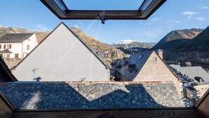 A view from a window with a skylight, overlooking a town with traditional buildings and mountains in the background.