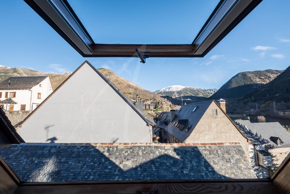 A view from a window with a skylight, overlooking a town with traditional buildings and mountains in the background.