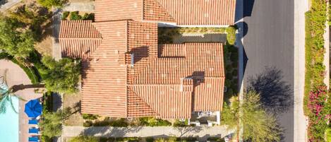 A residential area with terracotta-tiled roofs, a swimming pool, and a landscaped garden with pink flowers.