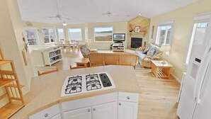 A spacious kitchen with a central island, a dining area with chairs, a sofa, and a TV. - Soundfront DogFriendly w Hot Tub, EV Charger, Private Sound Access, Beach Nearby (Frisco)