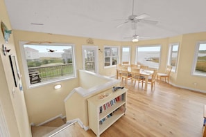 A spacious room with large windows, a ceiling fan, and a dining area with wooden chairs and a table.