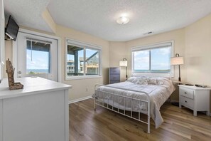 Ein Schlafzimmer mit Bett, Nachttischen, einem Schreibtisch und Fenstern mit Blick auf Gebäude und das Meer.