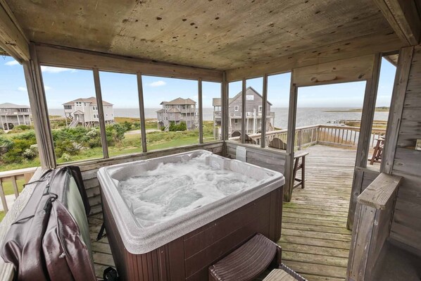 Um deck de madeira com uma banheira de hidromassagem, com vista para uma praia com casas.